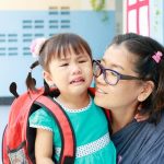 Toddler crying with separation anxiety while mother comforts her at school