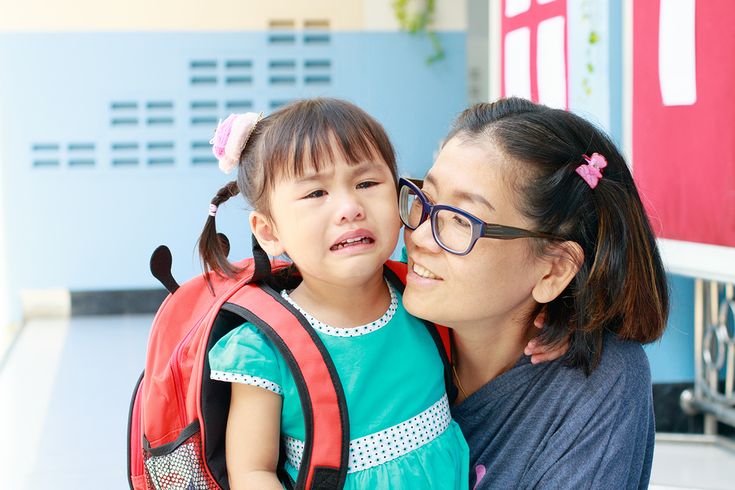 Toddler crying with separation anxiety while mother comforts her at school